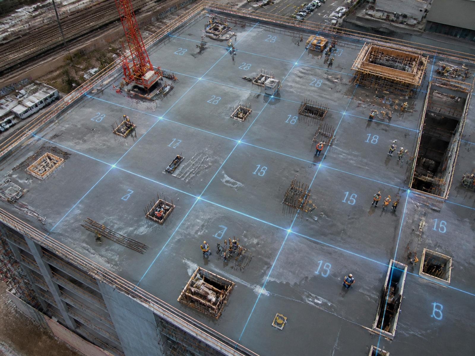 Aerial view of a slab deck divided into numbered work zones by blue laser grid lines with crews working in each