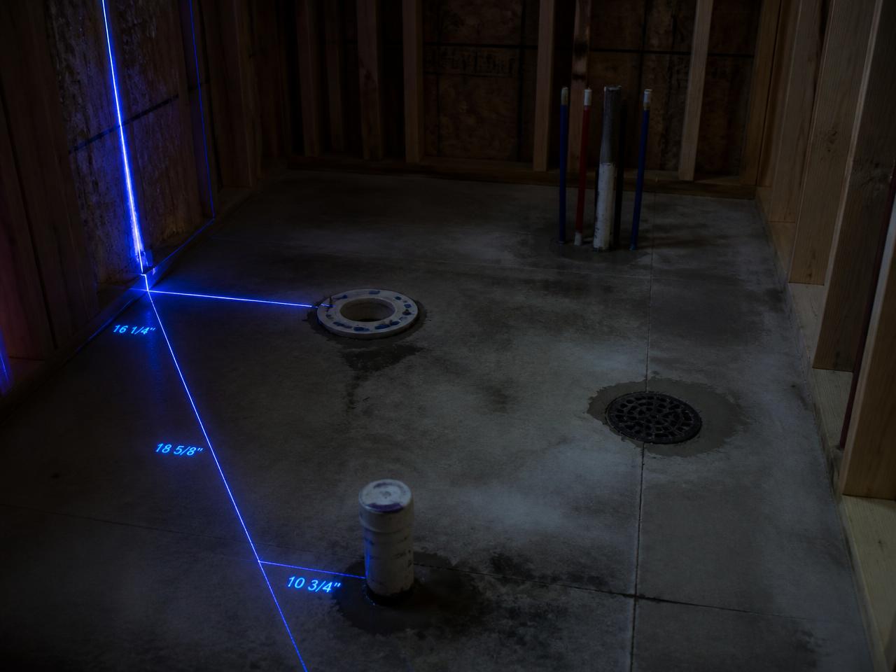 Bathroom rough-in slab with closet flange and drains measured by blue laser lines